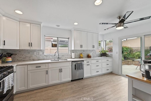 kitchen with a sink, stainless steel dishwasher, white cabinetry, light countertops, and gas range