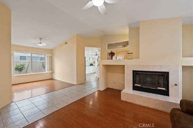 unfurnished living room featuring built in features, wood finished floors, a fireplace, ceiling fan, and vaulted ceiling