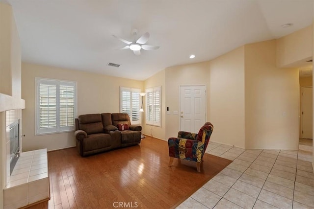 living room with light wood finished floors, visible vents, lofted ceiling, a tile fireplace, and a ceiling fan