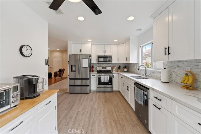 kitchen featuring tasteful backsplash, light wood-type flooring, stainless steel appliances, white cabinetry, and a sink