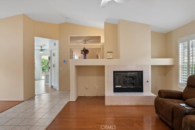 living area with wood finished floors, vaulted ceiling, a ceiling fan, and a tile fireplace