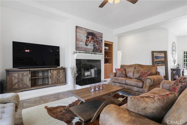 living room with a tile fireplace, ceiling fan, and built in shelves