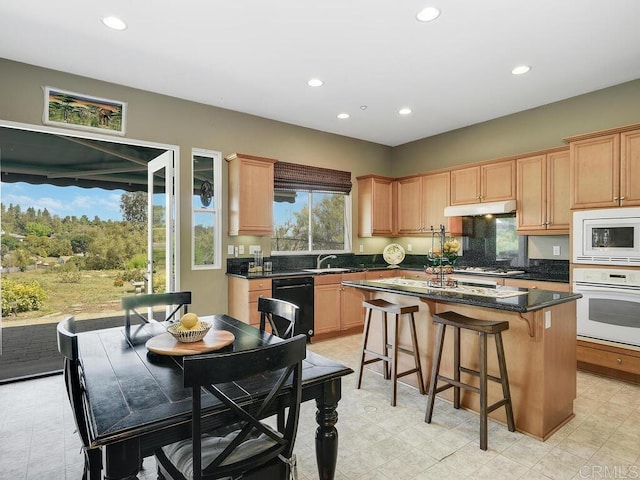 kitchen with sink, a breakfast bar area, a kitchen island, white appliances, and dark stone counters