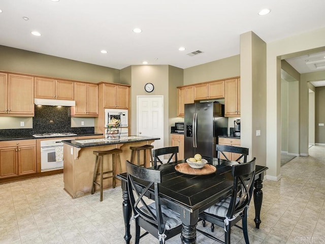 kitchen with a kitchen bar, tasteful backsplash, a kitchen island, white appliances, and dark stone counters