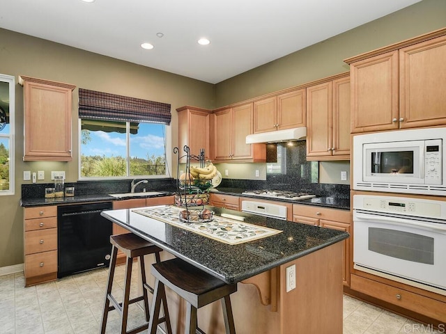 kitchen featuring a kitchen island, sink, a kitchen breakfast bar, dark stone counters, and white appliances