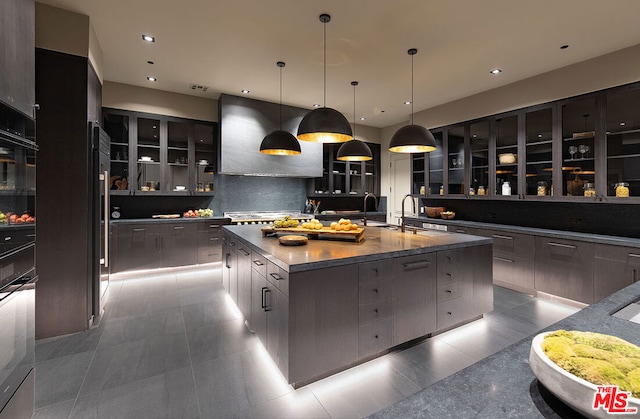 kitchen with backsplash, a large island with sink, ventilation hood, sink, and hanging light fixtures