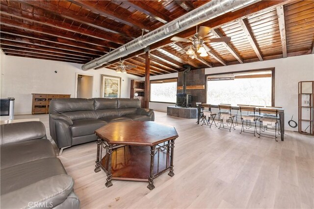 living room with a wood stove, ceiling fan, wooden ceiling, vaulted ceiling with beams, and light hardwood / wood-style floors