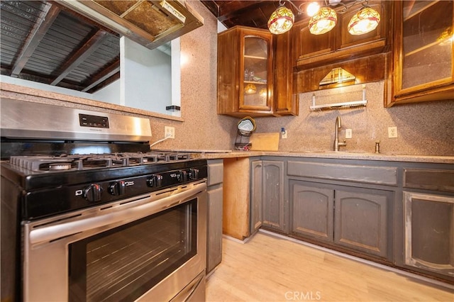 kitchen featuring stainless steel gas stove, beam ceiling, sink, and light hardwood / wood-style flooring