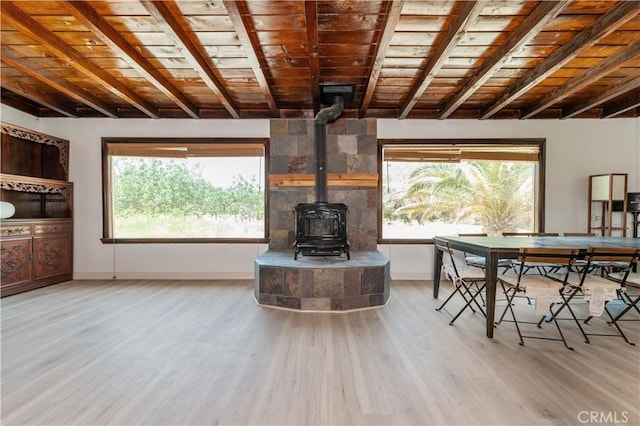 unfurnished living room featuring a wood stove, a wealth of natural light, wooden ceiling, and light wood-type flooring