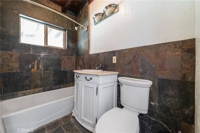 full bathroom featuring tiled shower / bath, vanity, toilet, and tile walls