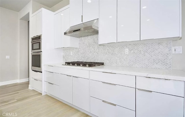 kitchen with white cabinets, light hardwood / wood-style flooring, decorative backsplash, light stone countertops, and stainless steel appliances