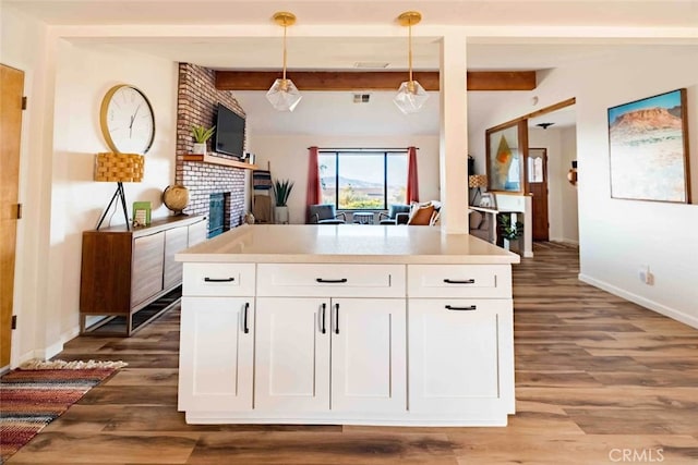 kitchen featuring a fireplace, hanging light fixtures, hardwood / wood-style flooring, white cabinetry, and beamed ceiling