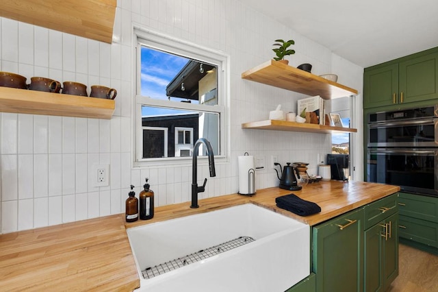 kitchen with double oven, green cabinets, sink, and butcher block countertops