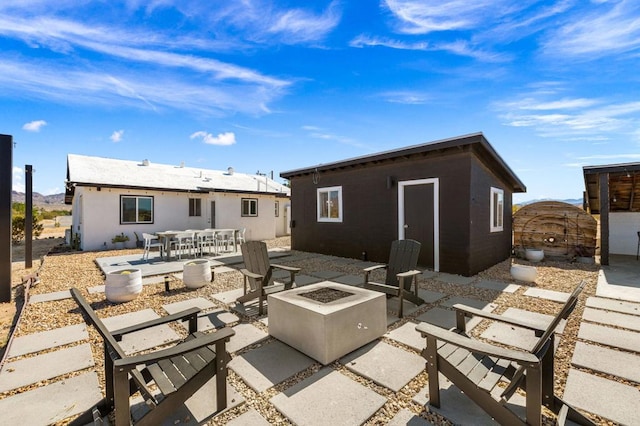 rear view of property with a fire pit, an outdoor structure, and a patio