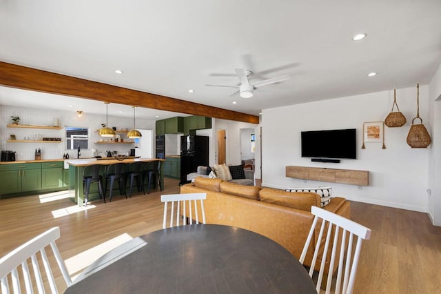 dining room featuring beam ceiling, light wood-type flooring, ceiling fan, and sink