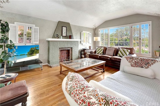 living room with a textured ceiling, a large fireplace, wood-type flooring, and vaulted ceiling