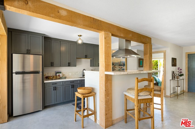 kitchen featuring stainless steel refrigerator, gray cabinetry, a kitchen bar, wall chimney exhaust hood, and sink