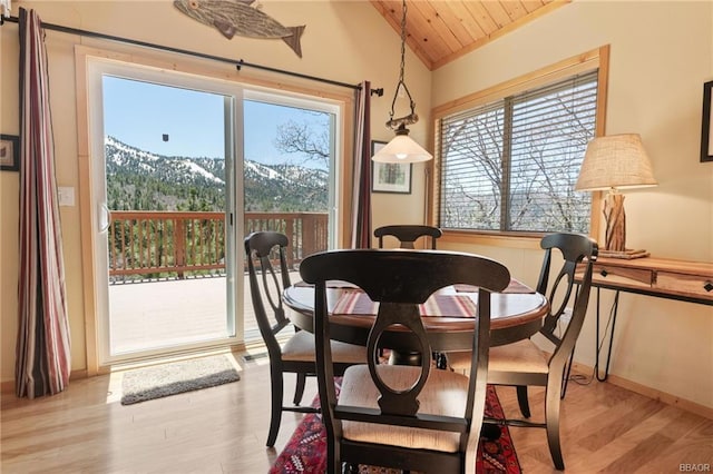 dining room with wood ceiling, light hardwood / wood-style floors, a mountain view, and lofted ceiling