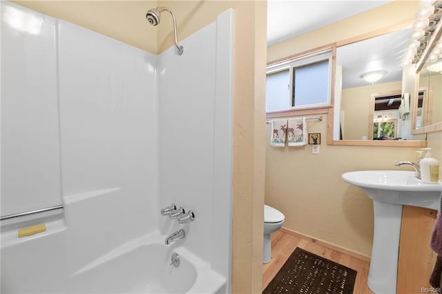 bathroom with washtub / shower combination, hardwood / wood-style flooring, and toilet