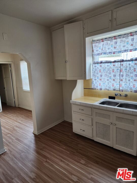 kitchen featuring tile counters, wood-type flooring, white cabinetry, and sink