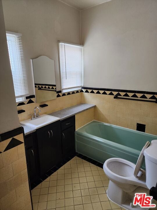 bathroom with tile walls, a washtub, toilet, tile flooring, and vanity