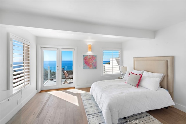 bedroom featuring access to exterior, a water view, and light hardwood / wood-style flooring