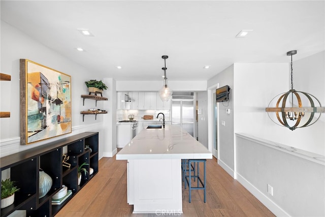 kitchen with high end appliances, sink, decorative light fixtures, light hardwood / wood-style flooring, and white cabinetry