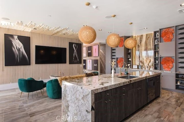 kitchen with decorative light fixtures, sink, a large island, light stone counters, and dark brown cabinets