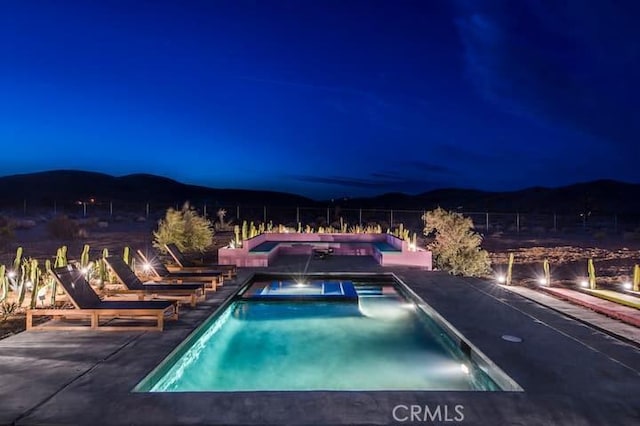 pool at twilight featuring a mountain view and an in ground hot tub