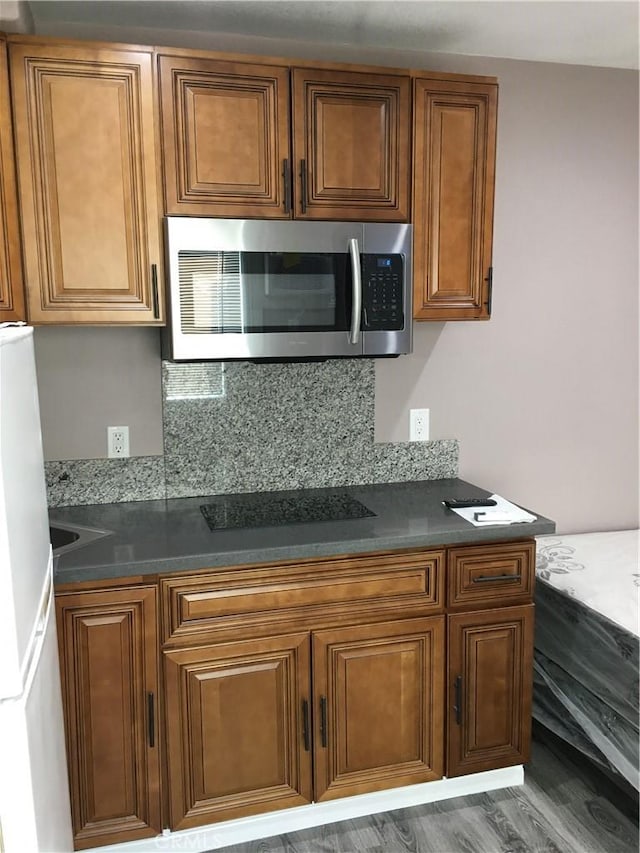 222 F St, Needles, CA 92363 - kitchen with stainless steel microwave, black electric stovetop, freestanding refrigerator, brown cabinetry, and dark countertops