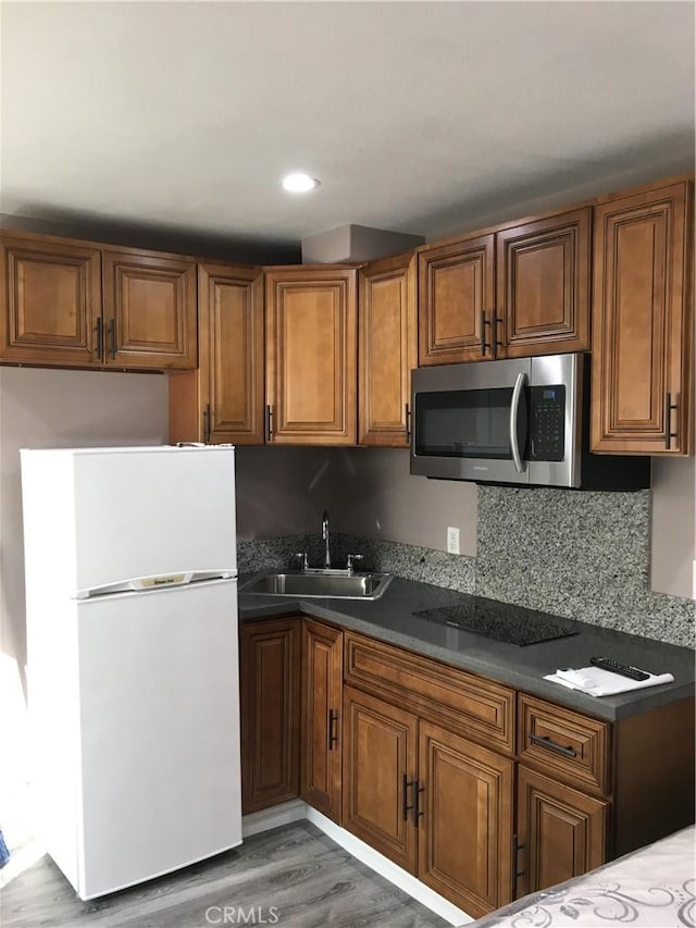 222 F St, Needles, CA 92363 - kitchen with stainless steel microwave, freestanding refrigerator, a sink, black electric cooktop, and brown cabinetry