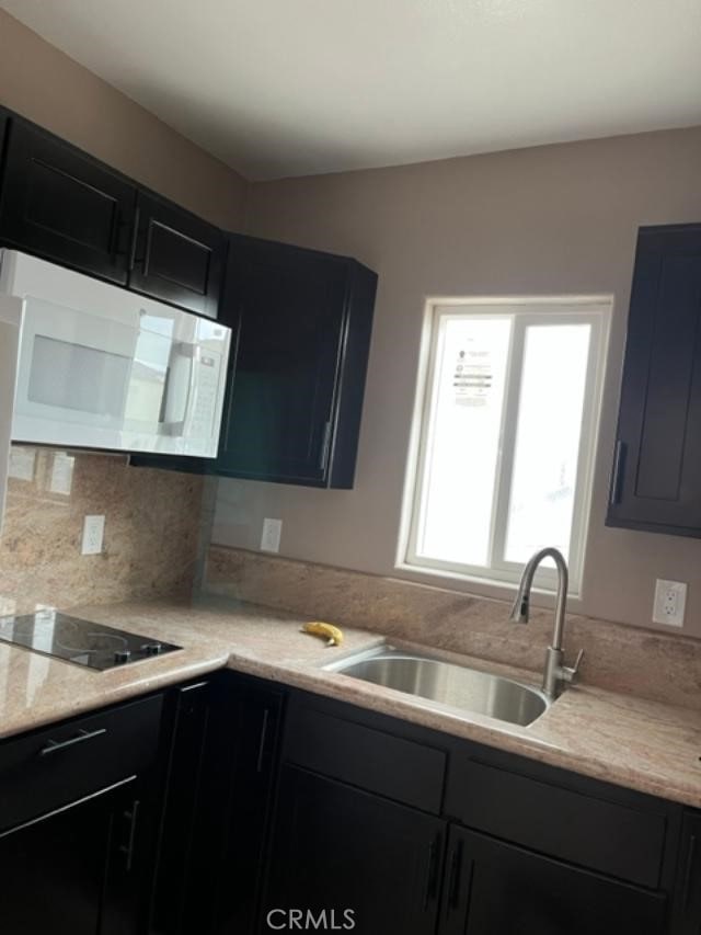 222 F St, Needles, CA 92363 - kitchen with white microwave, a sink, black electric stovetop, dark cabinetry, and backsplash