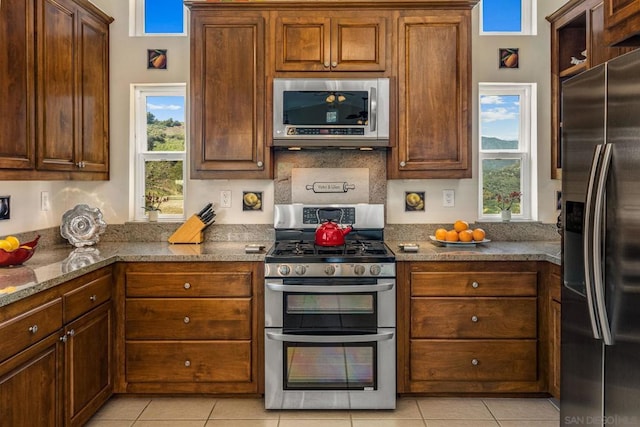 kitchen featuring light stone countertops, appliances with stainless steel finishes, light tile patterned floors, and a wealth of natural light