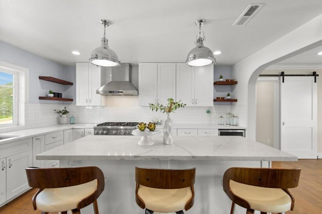 kitchen featuring white cabinets, a barn door, wall chimney range hood, and stove