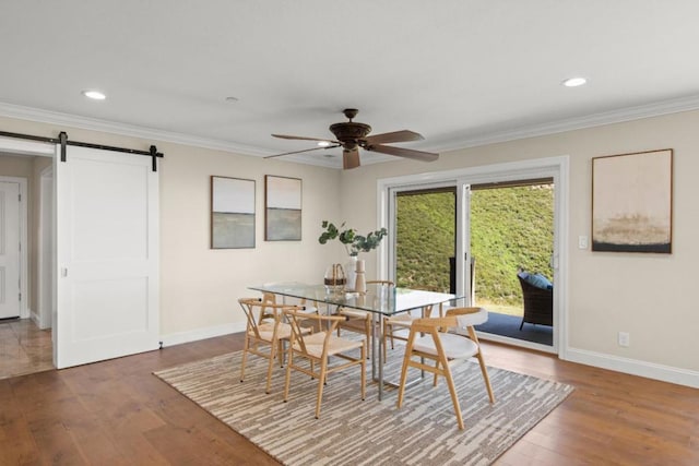 dining room with ceiling fan, a barn door, dark hardwood / wood-style flooring, and ornamental molding