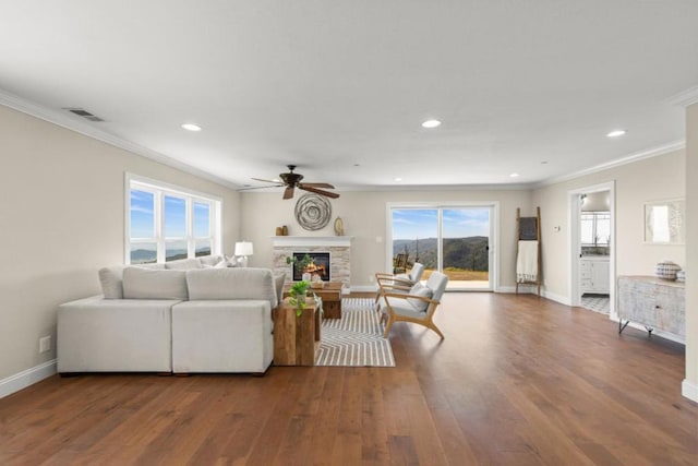 living room with ceiling fan, hardwood / wood-style floors, crown molding, and a stone fireplace