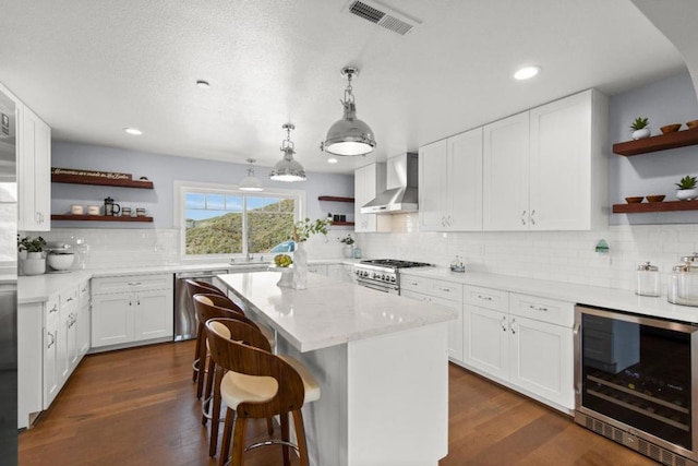 kitchen featuring appliances with stainless steel finishes, beverage cooler, wall chimney range hood, white cabinets, and a center island