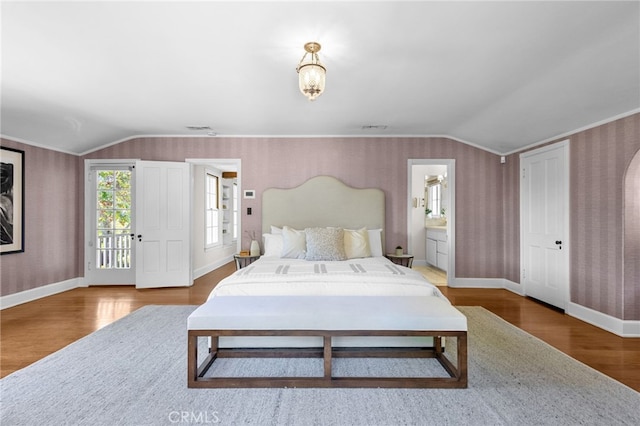 bedroom featuring ensuite bathroom, wood-type flooring, and vaulted ceiling