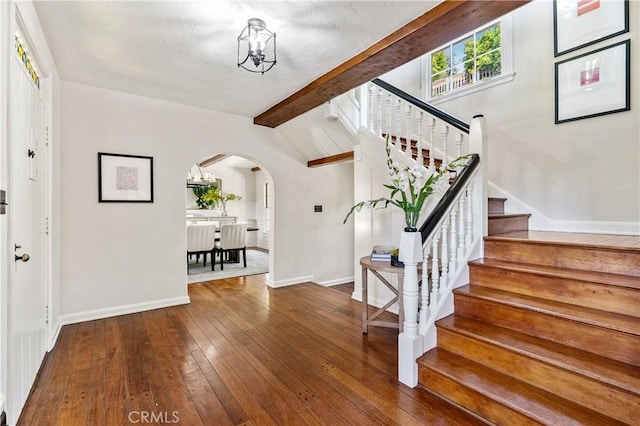 foyer with hardwood / wood-style floors, vaulted ceiling with beams, and a chandelier