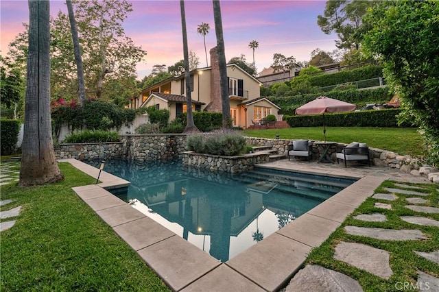 pool at dusk featuring a lawn and a patio area