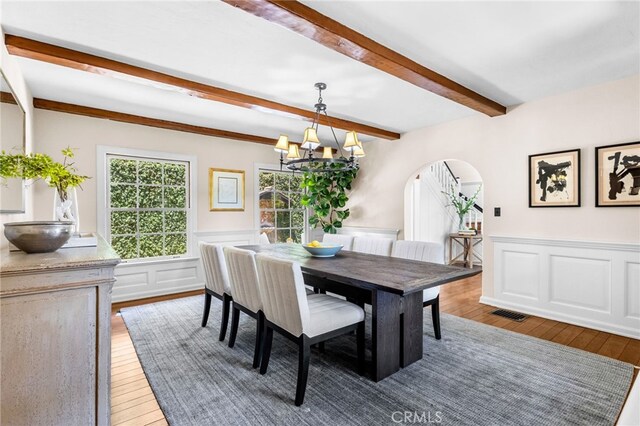 dining room with beamed ceiling, wood-type flooring, and a chandelier