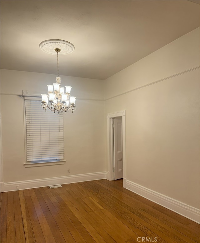 spare room with a notable chandelier and dark wood-type flooring