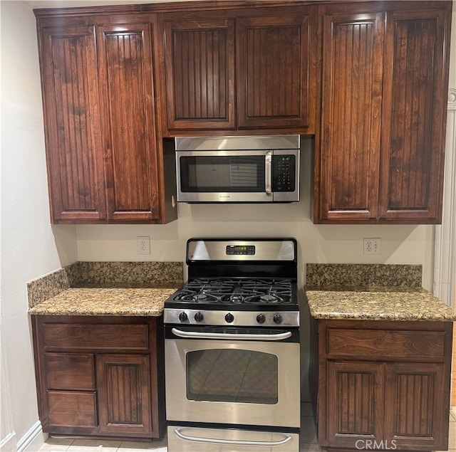 kitchen with dark brown cabinetry, stainless steel appliances, and light stone counters