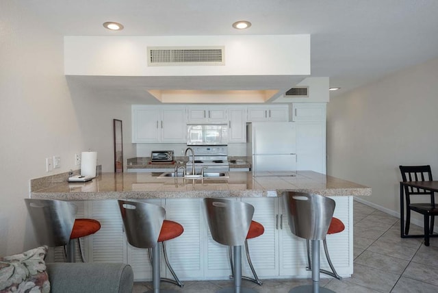 kitchen with white cabinets, sink, white appliances, kitchen peninsula, and a kitchen breakfast bar