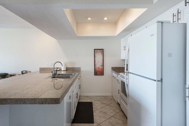 kitchen featuring white appliances, light tile flooring, white cabinets, sink, and a raised ceiling