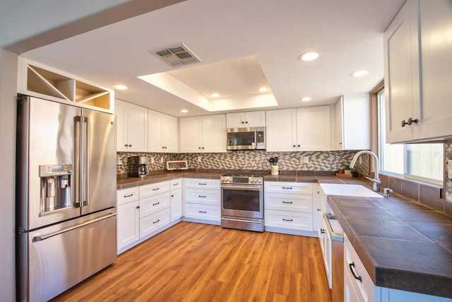 kitchen featuring light wood-type flooring, stainless steel appliances, a raised ceiling, sink, and white cabinetry