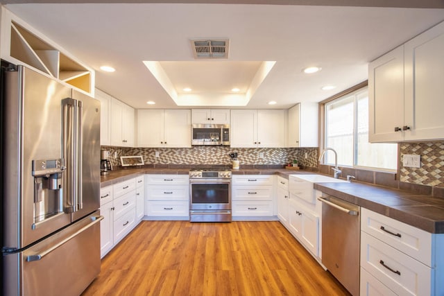 kitchen featuring sink, a raised ceiling, appliances with stainless steel finishes, white cabinets, and light wood-type flooring