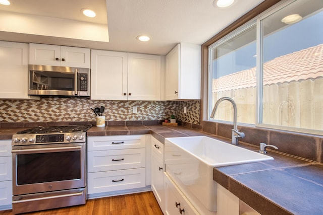 kitchen featuring white cabinets, light wood-type flooring, appliances with stainless steel finishes, and tasteful backsplash