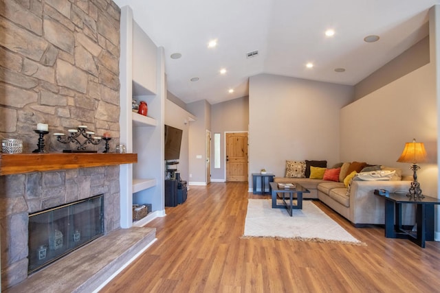 living room featuring built in features, a fireplace, lofted ceiling, and light wood-type flooring