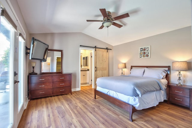 bedroom with ceiling fan, a barn door, ensuite bathroom, light hardwood / wood-style floors, and vaulted ceiling